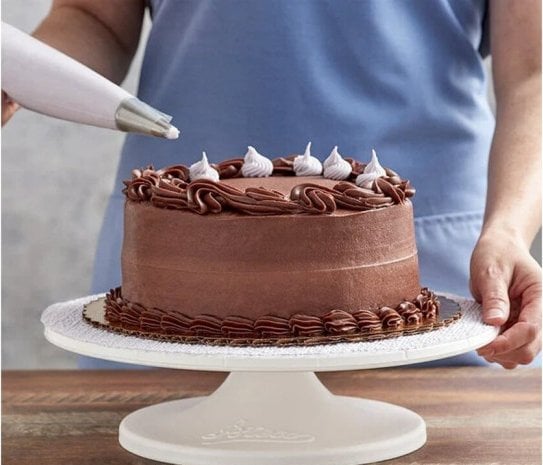 Piping meringue decorations onto a chocolate cake on an Ateco revolving cake stand